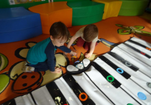Dwóch chłopców losuje jedną z figur geometrycznych, która znajduje się na instrumencie Kolorpiano.